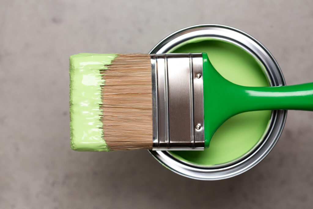 Paintbrush On Metal Bucket With Green Pigment For Renovation Works On Concrete Gray Background. Redecoration Concept In Home Interior. Flat Lay Style And Close Up