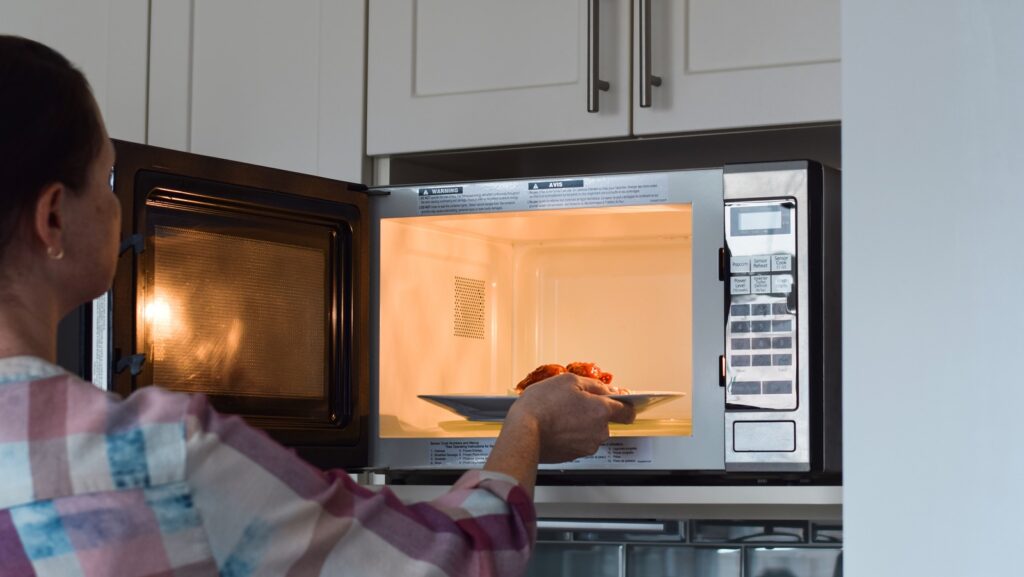 Woman,placing,plate,with,food,into,microwave,to,warm,up