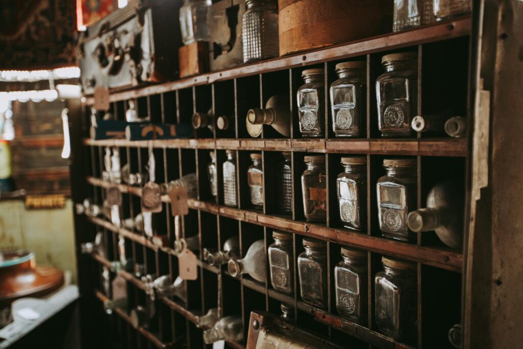 Rustic collection of vintage glass bottles neatly arranged on wooden shelves in an antique store.