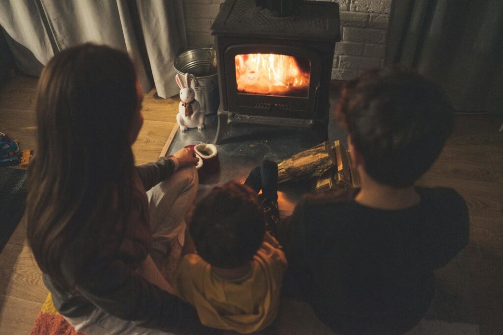 From above back view of anonymous children sitting near fireplace with burning firewood in cozy living room in evening time