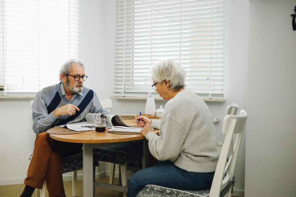 Elderly couple reading newspapers and having coffee together in a bright dining room.