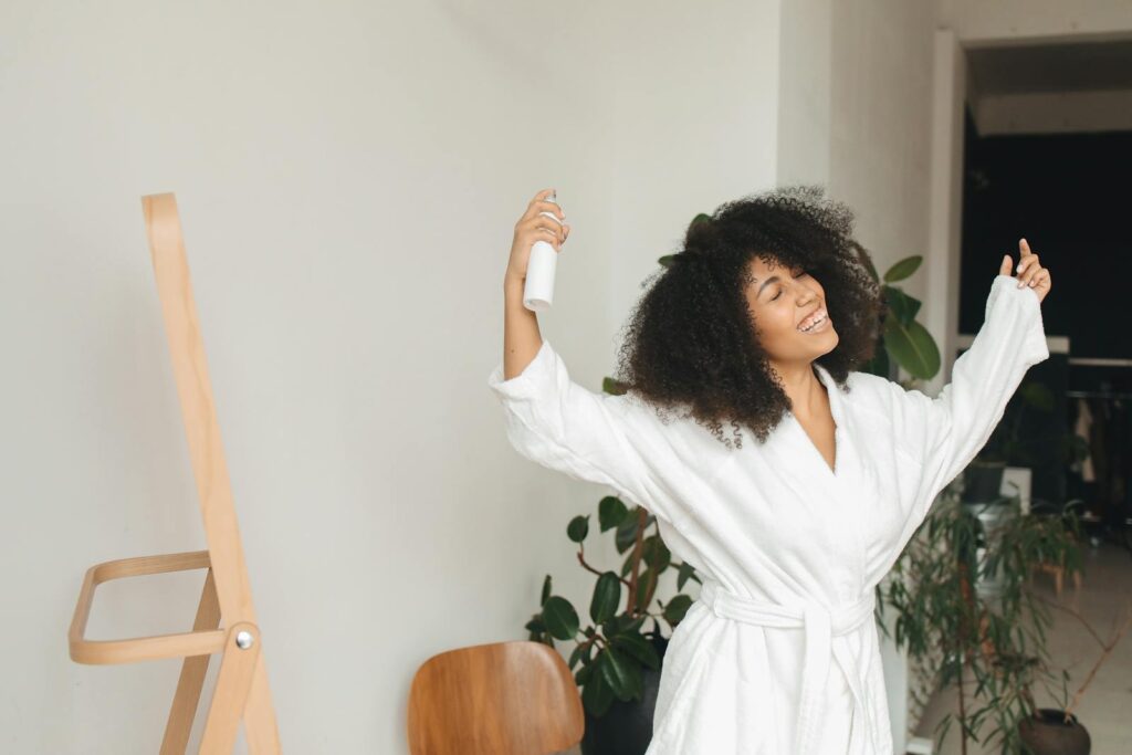 Happy woman with curly hair in bathrobe enjoying morning routine indoors.