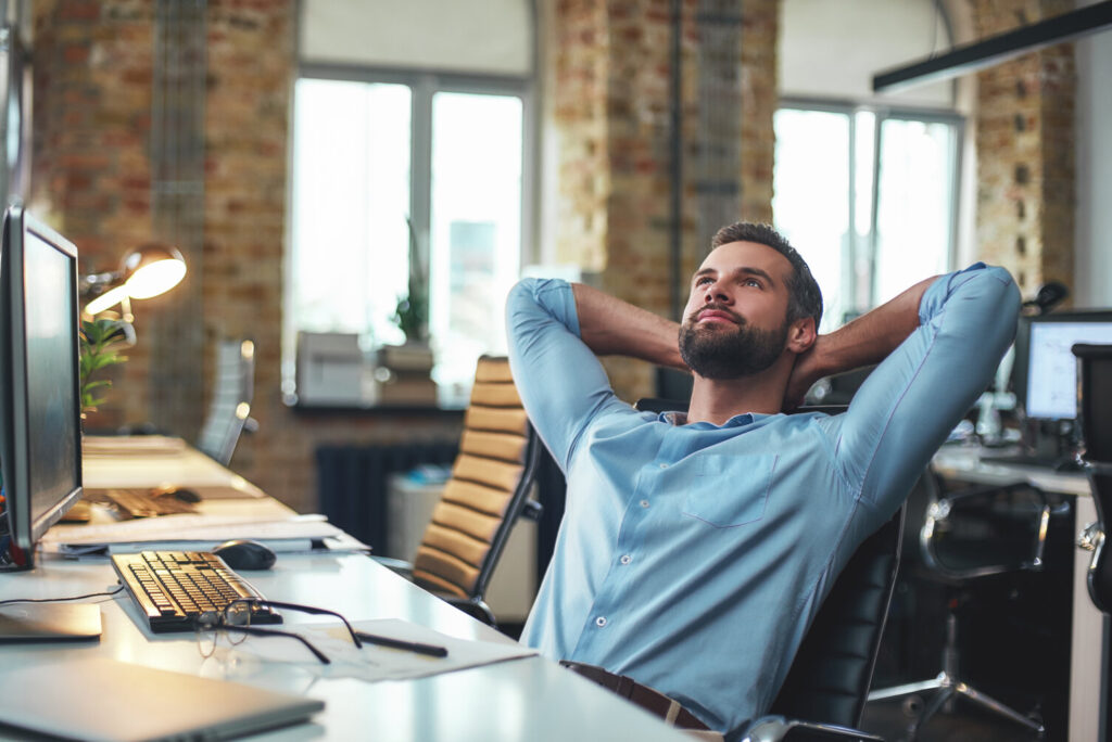 Enjoying Break. Satisfied Young Bearded Businessman Leaning Back With Hands Behind Head And Relaxing While Sitting In The Modern Office