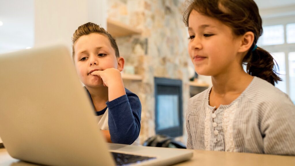 Brother And Sister Watching Cartoons On A Laptop In The Kitchen During Breakfast