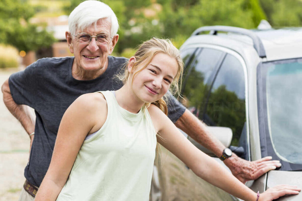 Senior Man, Grandfather And His 13 Year Old Grand Daughter Washing A Car Together In Driveway