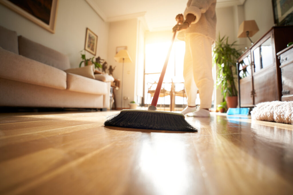 Unrecognizable Woman Sweeping The Parquet Floor, Window Light Reflection.