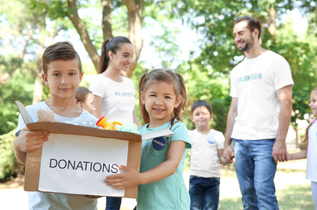 Young Volunteers And Children With Box Of Donations Outdoors