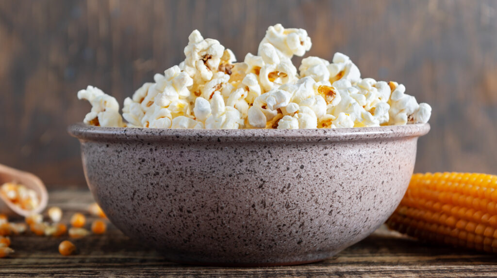 Freshly Cooked Popcorn In A Bowl On A Wooden Table. Traditional American Maize Snack.