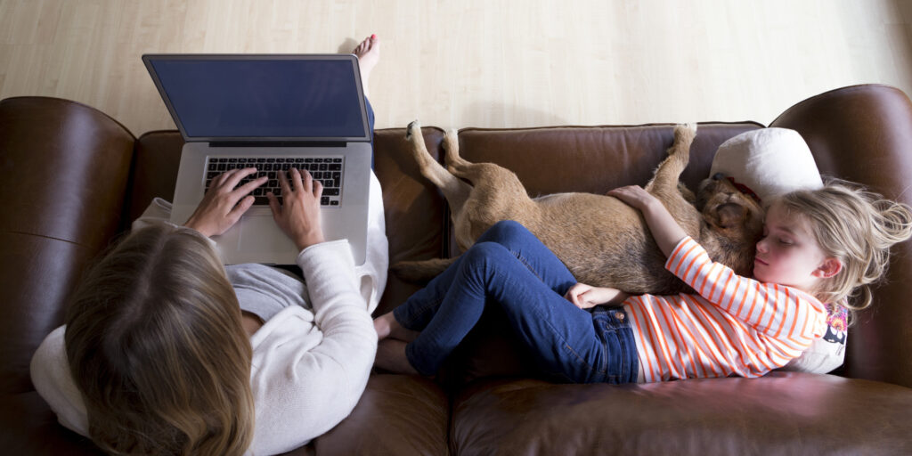 Woman Using Laptop While Daughter And Dog Sleep