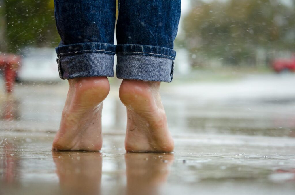 Close-up of bare feet on a wet pavement, capturing calm and connection with nature.