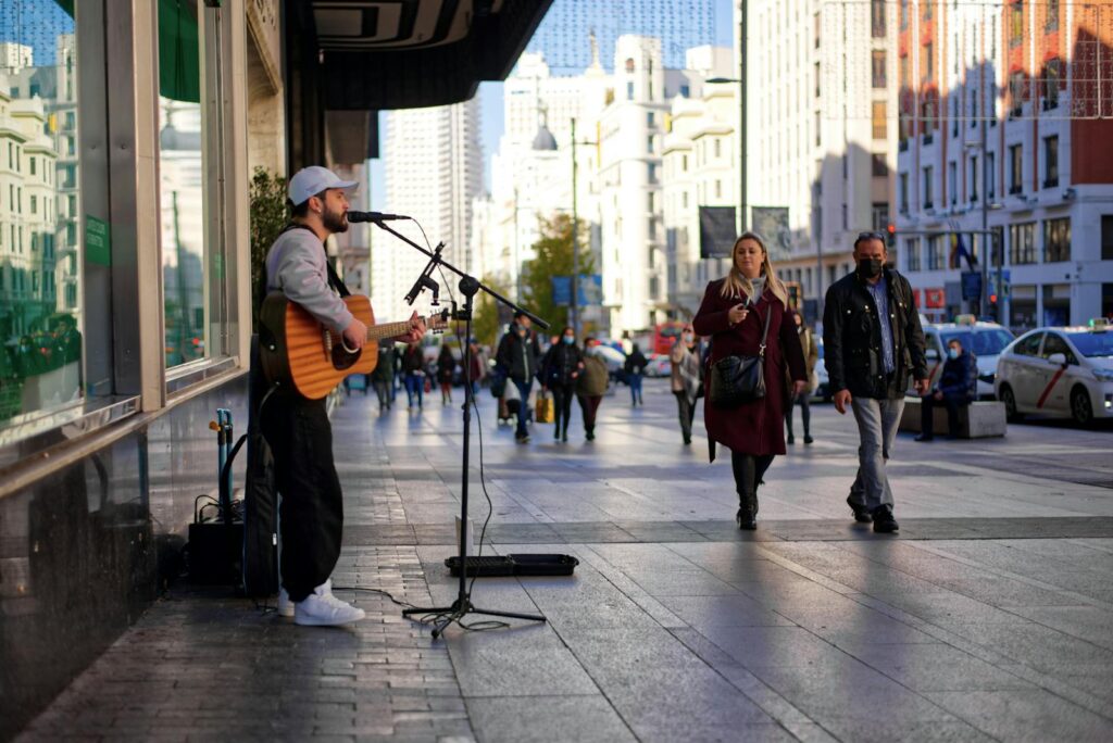 A street musician plays guitar and sings on a busy sidewalk in Madrid, Spain.