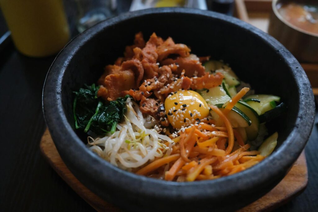 Delicious Korean bibimbap in a hot stone bowl with fresh ingredients like vegetables and egg yolk.