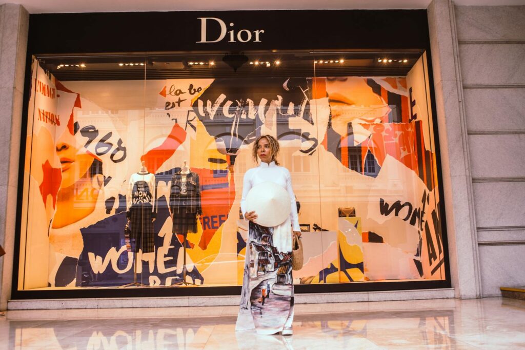 Elegant woman in traditional ao dai poses in front of chic Dior storefront display.