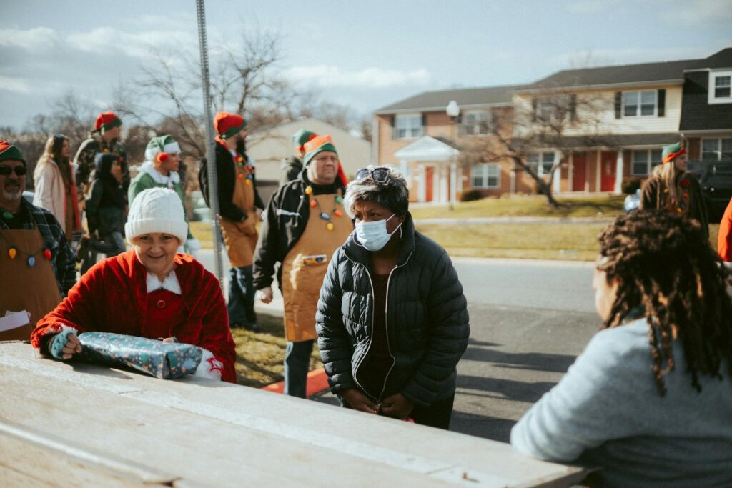 A neighborhood holiday gathering featuring adults dressed in elf costumes distributing gifts on a street.