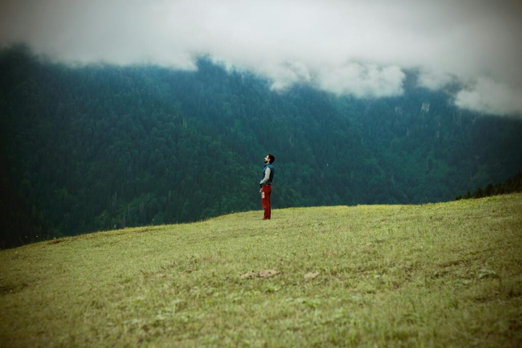 A solitary man gazes at clouds while standing on a vast mountainside.