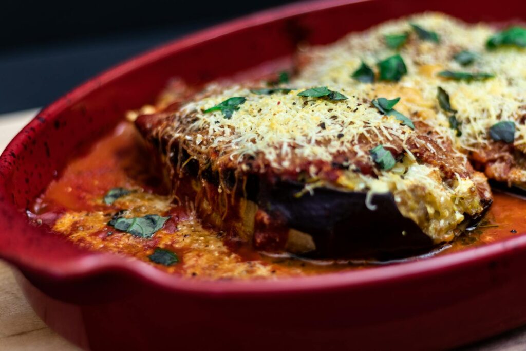 Delicious baked eggplant parmesan dish with cheese and tomato sauce in a red tray.