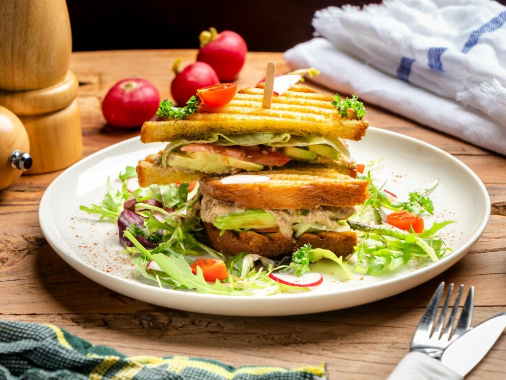 Close-up of a gourmet tuna sandwich with fresh vegetables on a rustic wooden table.
