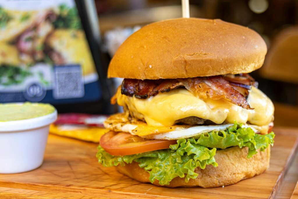 Close-up of a delicious bacon cheeseburger with lettuce, tomato, and cheese on a wooden board.