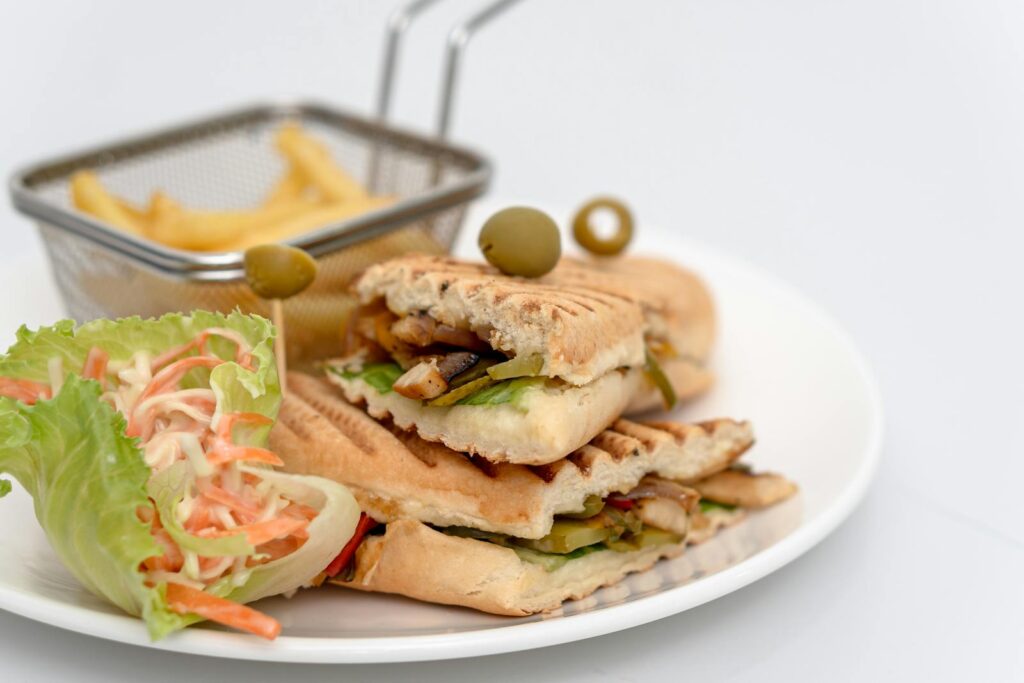 Grilled panini with veggies, served with French fries and a fresh salad on a white plate.