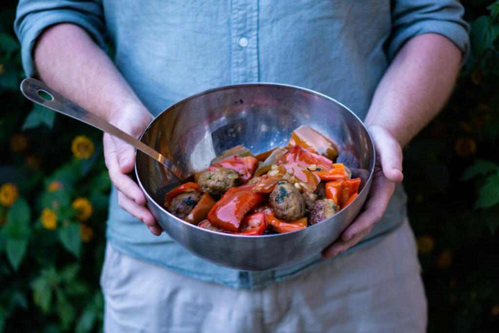 Delicious homemade ratatouille and meatballs served in a large bowl, held outdoors against a natural backdrop.