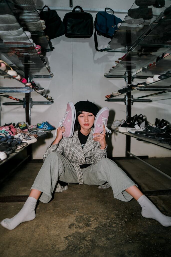 A young woman sits on the floor of a shoe store holding sneakers in a trendy and casual pose.