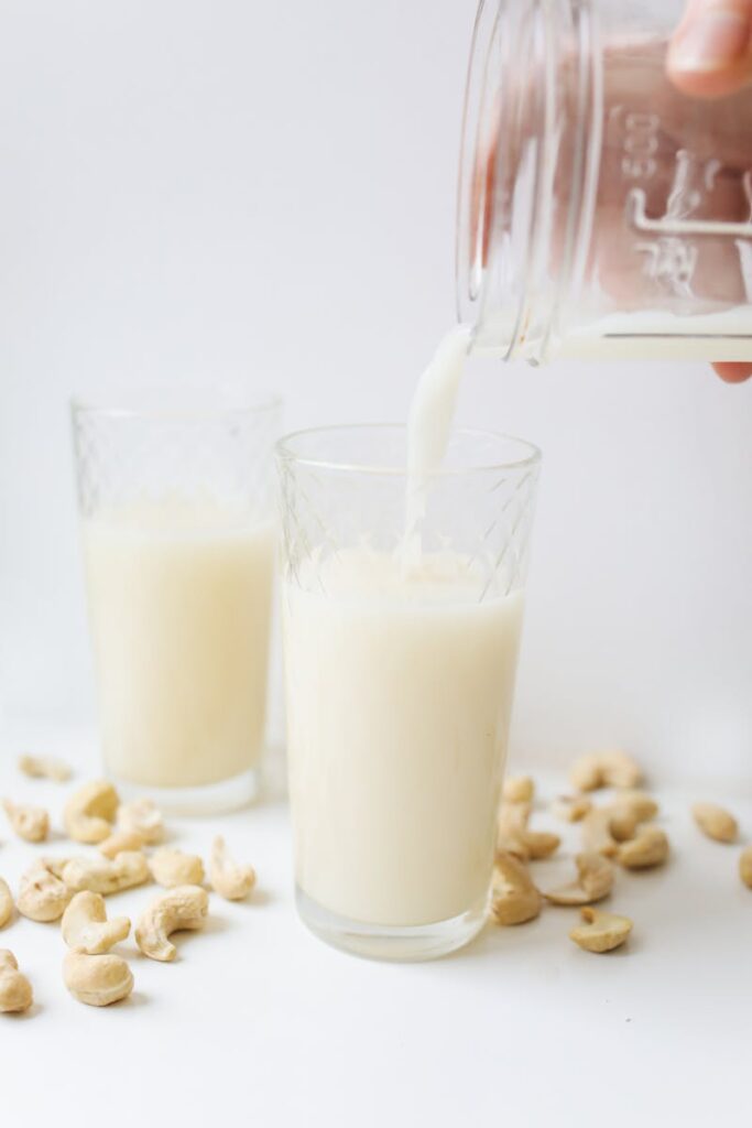 Delicious cashew milk being poured into a glass surrounded by cashews, showcasing refreshing plant-based nutrition.