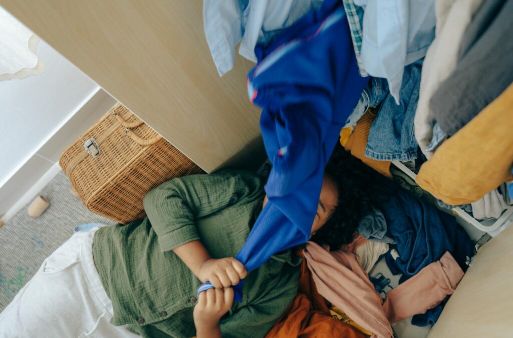 Teenager lying amidst a cluttered closet filled with diverse apparel, showing an untidy and playful atmosphere.