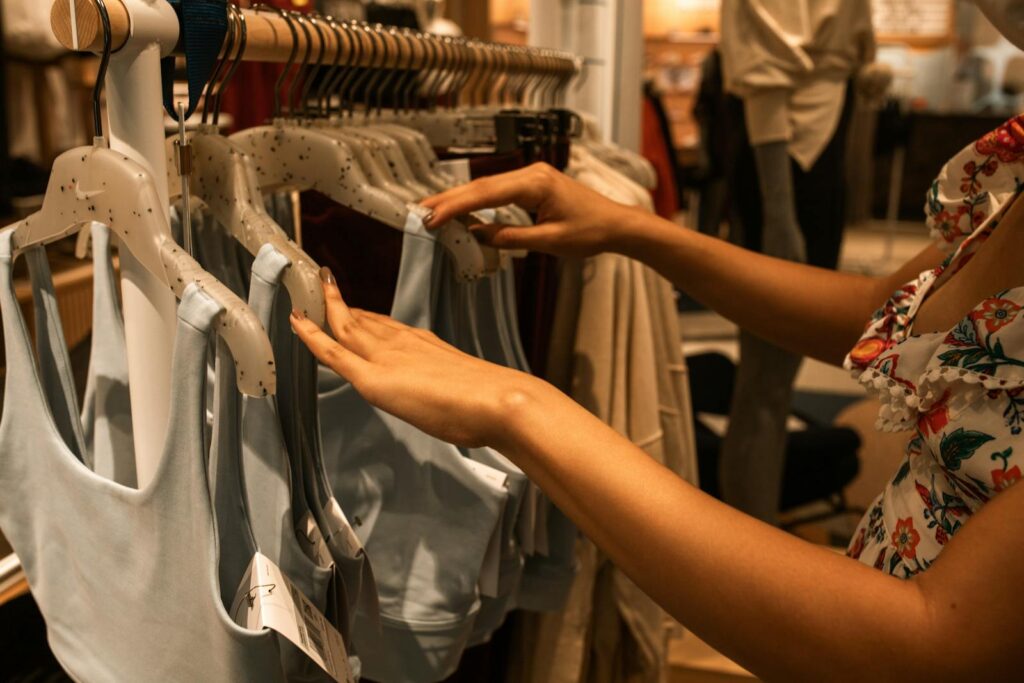 A woman selecting blue tops from a clothing rack inside a fashion boutique.