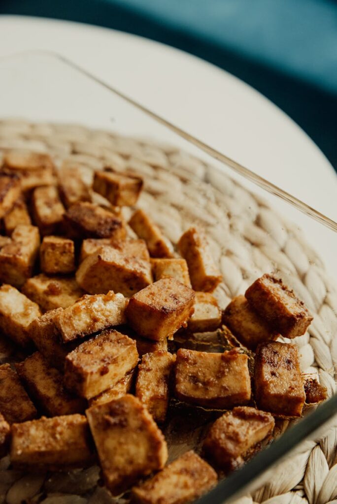 Close-up of crispy baked tofu cubes in a glass dish on a woven mat, perfect for vegan recipes.