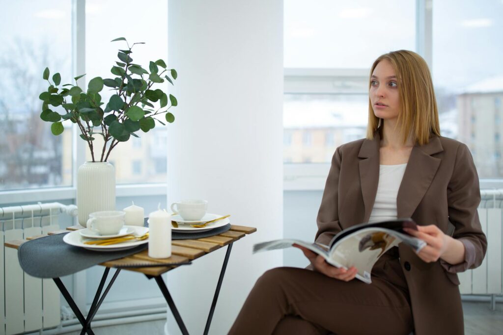 Young woman in business attire reads a magazine while enjoying a coffee break indoors.
