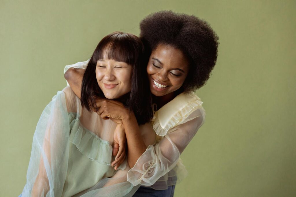 Two women joyfully embracing in a studio setting with a soft green background.