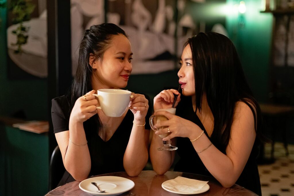 Two women enjoying drinks at a caf&eacute;, sharing a special moment together.