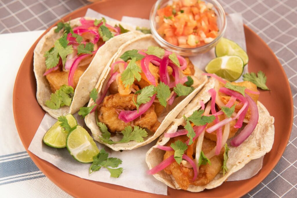 Delicious fish tacos garnished with pickled onions and cilantro, served with lime and salsa.