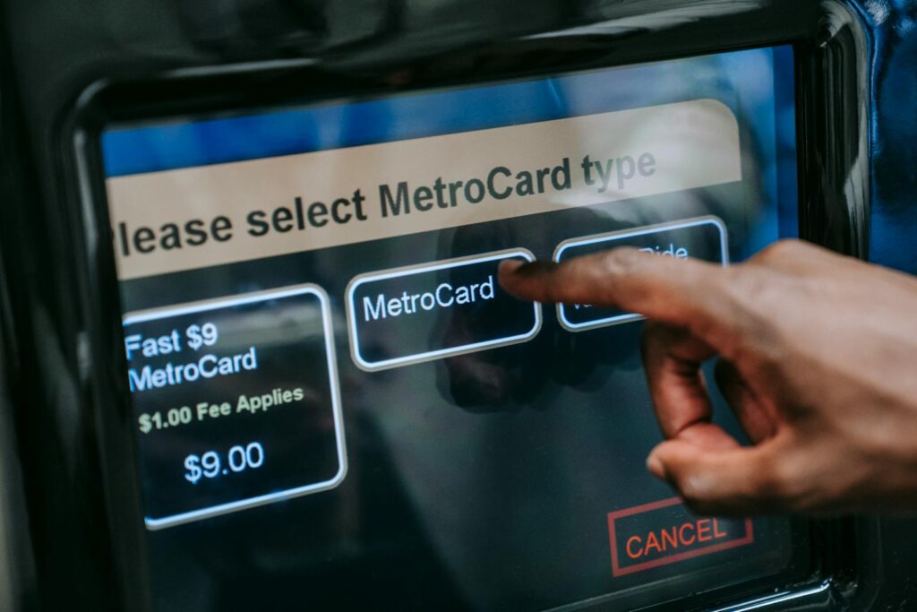 Close-up of a hand selecting a MetroCard type on a touchscreen in a subway station.