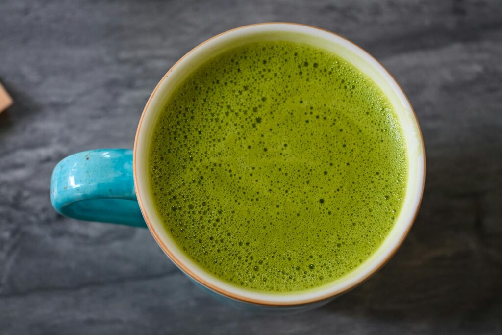 A top view of a ceramic cup filled with frothy green matcha latte on a dark surface.