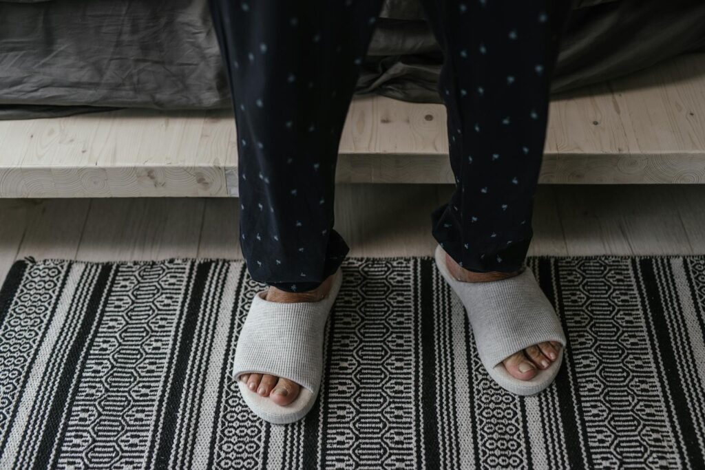 A person stands in soft slippers and polka dot pajamas on a patterned rug.