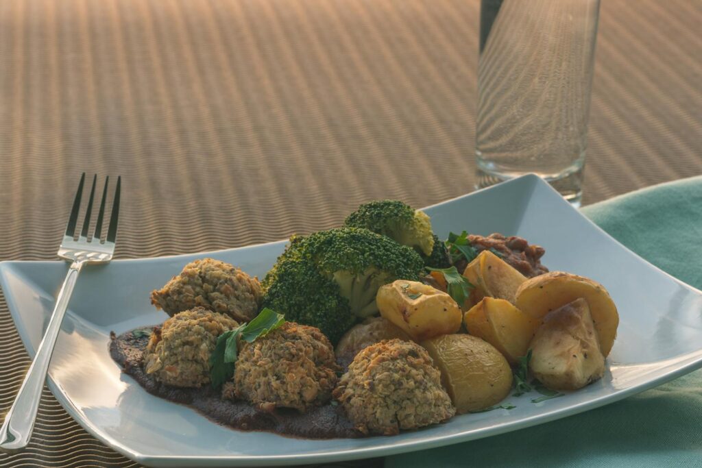 A close-up of a healthy vegan meal with baked potatoes, broccoli, and falafel on a white plate.