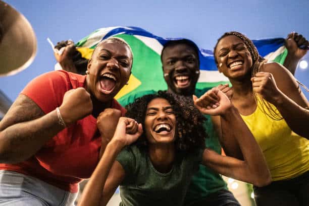 Portrait Of Friends Celebrating With South African Flag Outdoors
