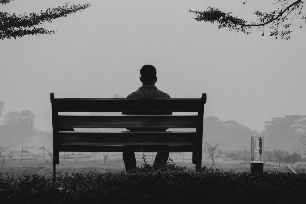 A solitary man sits on a bench in Dhaka, Bangladesh, silhouetted against a foggy, grayscale landscape.