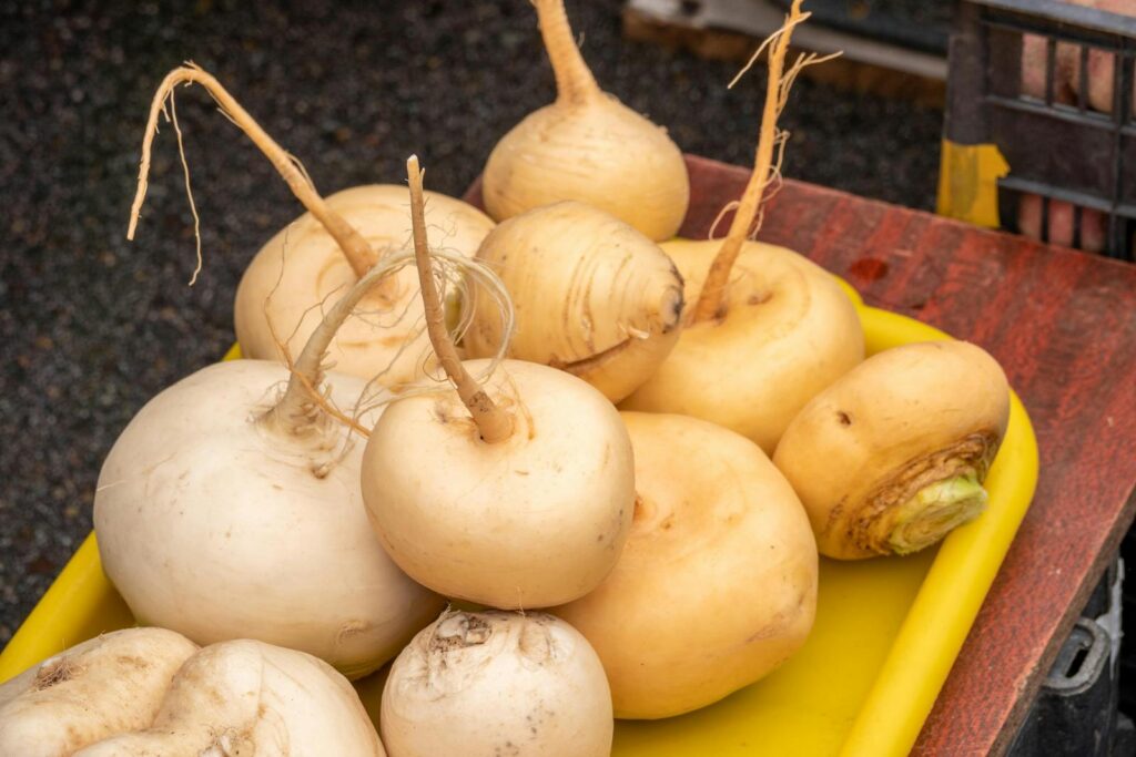 A variety of fresh turnips displayed on a yellow tray at a farmers market.