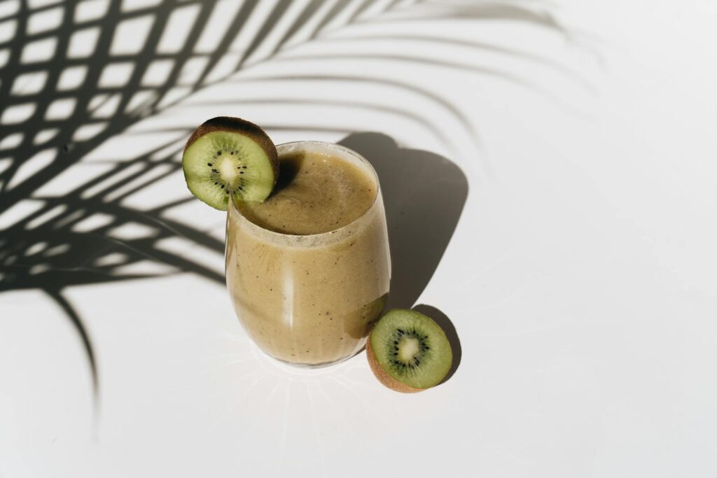 A vibrant kiwi smoothie with palm leaf shadows creating a tropical feel.