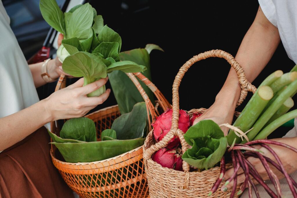 Close-up of hands holding wicker baskets filled with fresh vegetables and fruits outdoors.