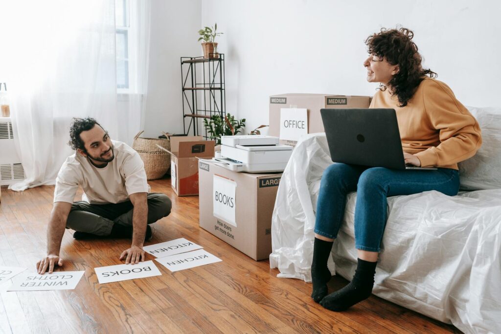 A couple organizing and packing boxes in their new home, using labels and a laptop.