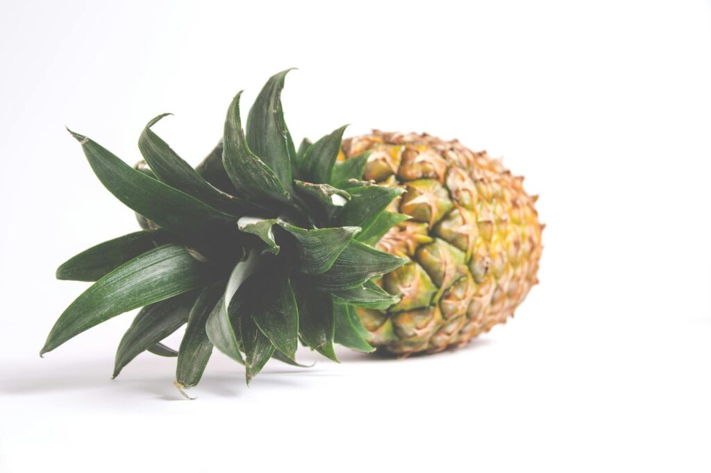 A single ripe pineapple with vibrant green leaves set against a white background, showcasing freshness.