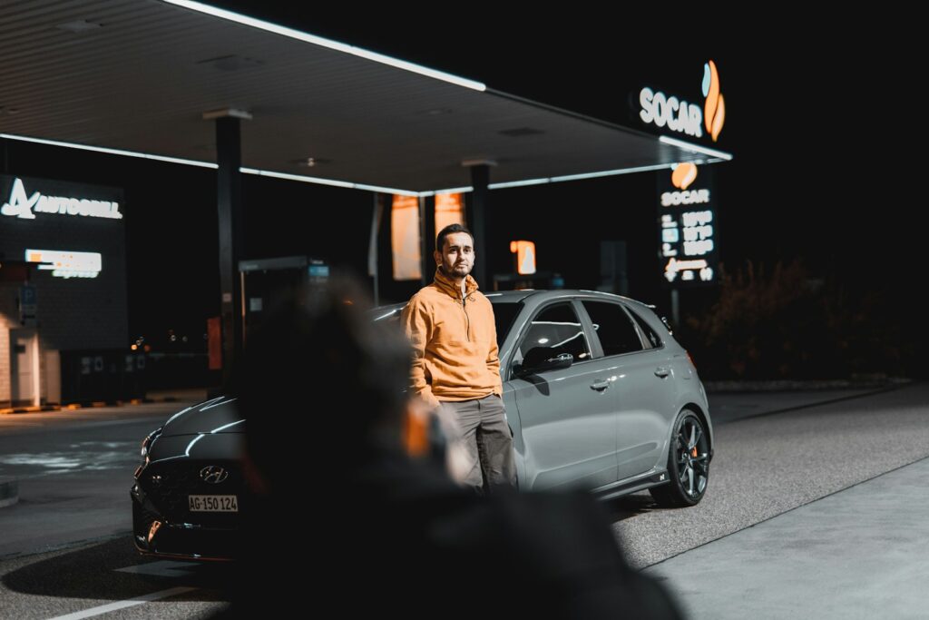 a man standing next to a car in front of a gas station