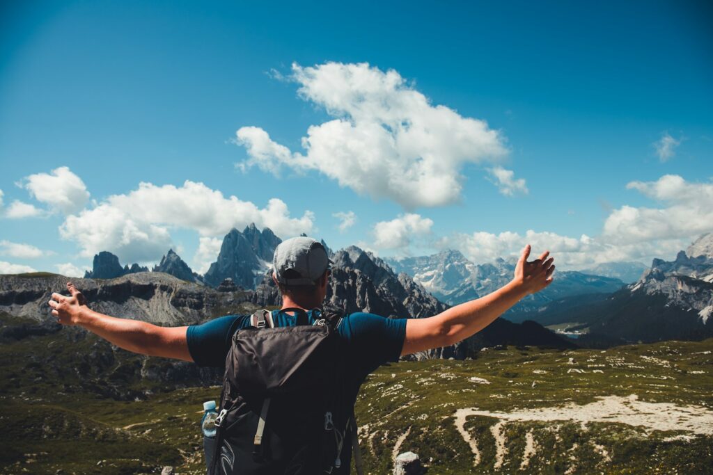 man in black t-shirt and black backpack standing on mountain under blue sky and white