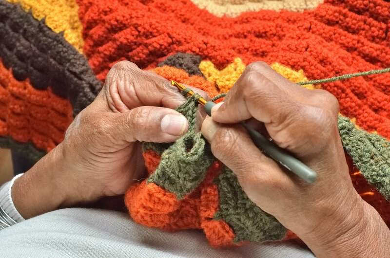 A person knitting a blanket with a pair of scissors