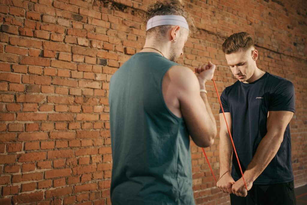 Two men exercising with resistance bands against a brick wall background, showcasing fitness and concentration.