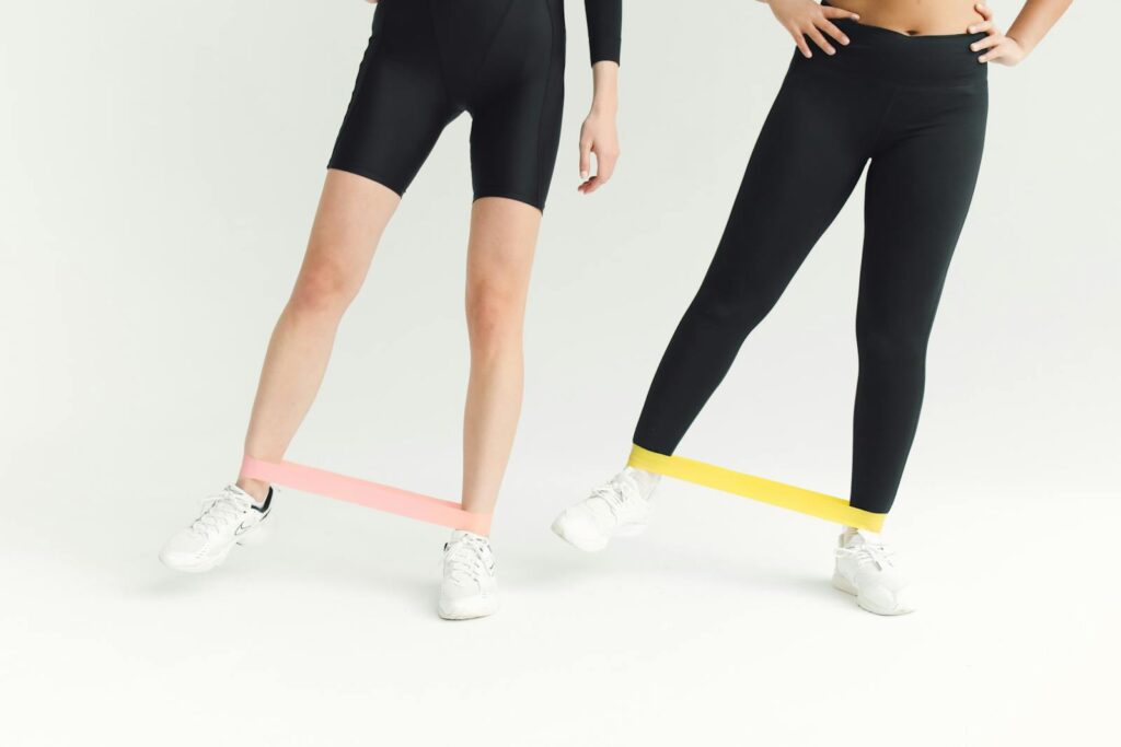 Two women exercising with resistance bands, focusing on leg workouts in a minimalistic setting.