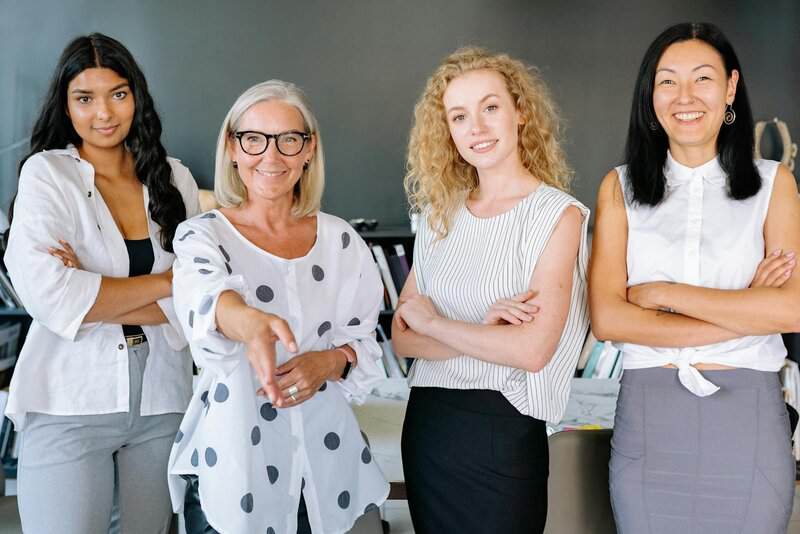 Smiling diverse group of businesswomen, arms crossed, in modern office setting.
